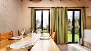 A dining area with a wooden table set for six, chairs, and a view of a garden through large windows. - Holiday Home in Peaceful Setting and Large Garden (Rendeux)