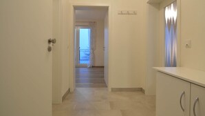 Un corridoio con una porta a sinistra, una scala che conduce a un balcone e un armadietto bianco a destra.
