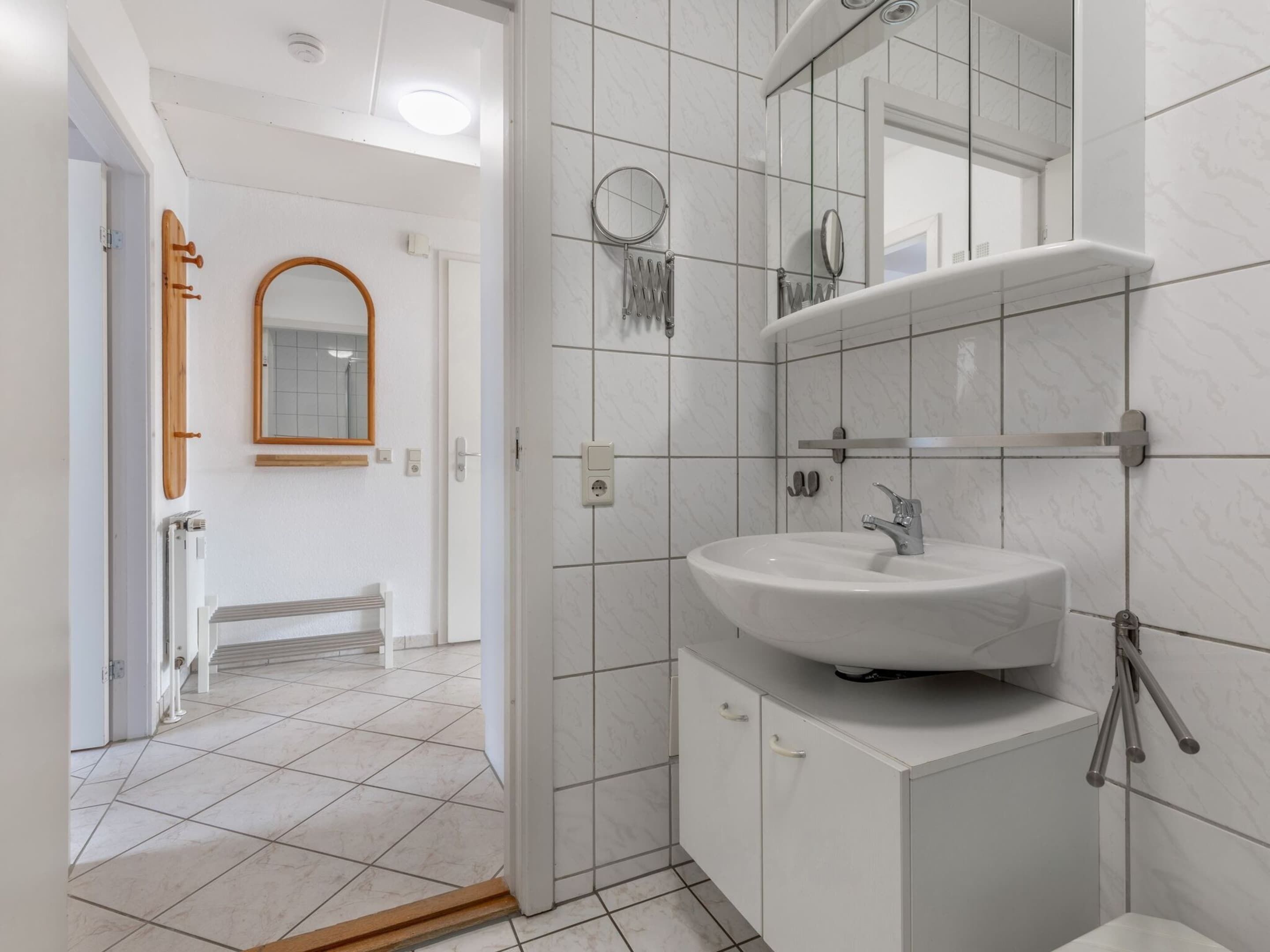Un bagno moderno con lavandino bianco, specchio e pareti rivestite di piastrelle.