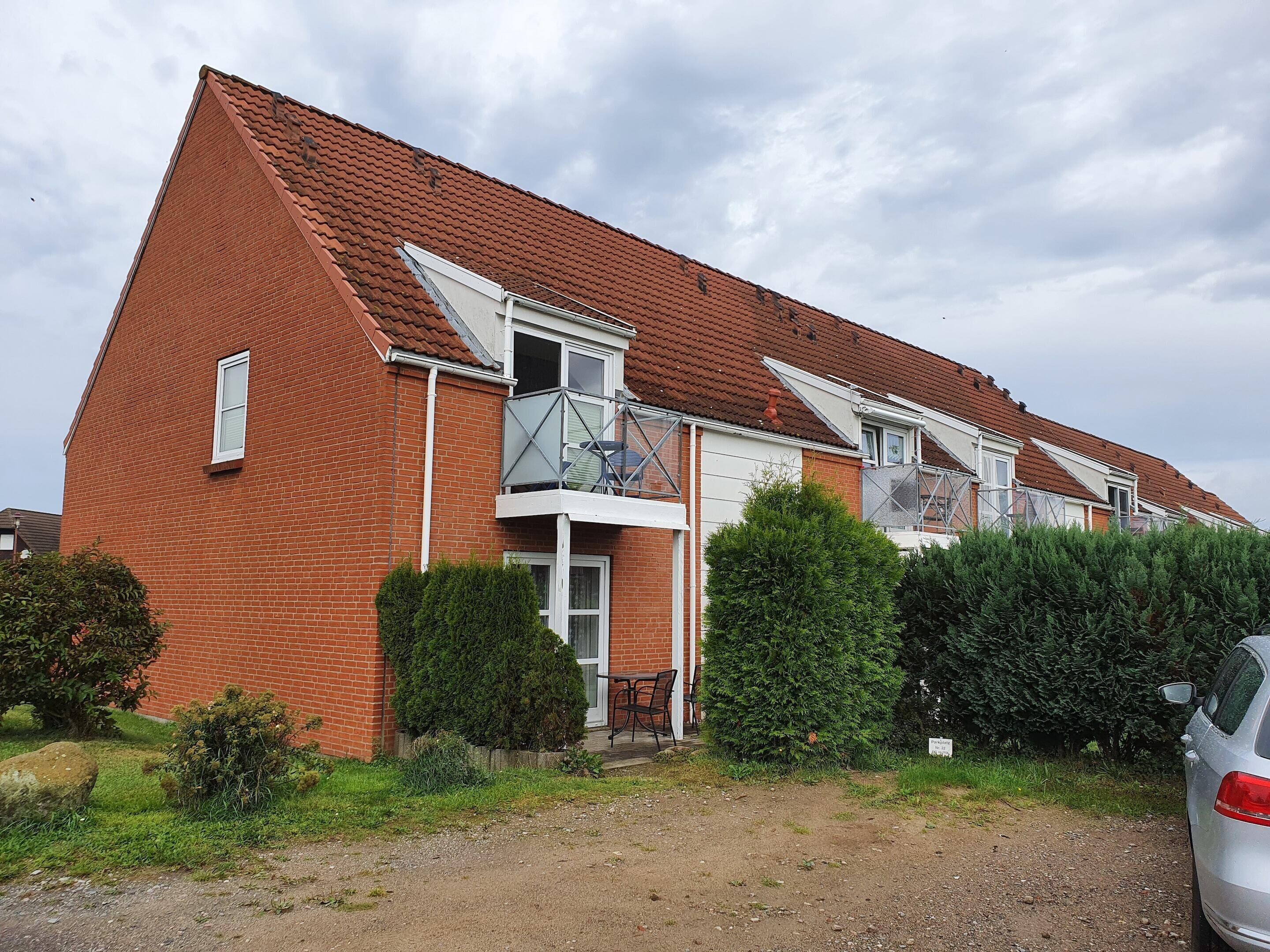 A two-story brick house with a sloped roof, a balcony with glass railings, and a small front garden.
