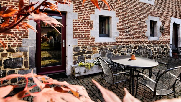 A brick building with a stone facade, a round table with chairs, and a door with a window. - Nice Apartments in a Monumental Square Farm (Vise)