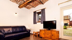 A living room with a leather sofa, a wooden cabinet with a flat-screen TV, a small table, and a window with checkered curtains. - Nice Apartments in a Monumental Square Farm (Vise)