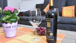 A bottle of GIORDANO VATO 94 TOSCANA ROSSOT wine, a glass, and a purple pot with pink flowers on a table. - Gemutliches Familienapartment (Werda)