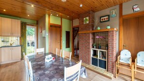 A dining area with a table, chairs, a brick fireplace, and a kitchen in the background. - Pretty Holiday Home near Durbuy & La Roche-en-Ardennes (Erezee)