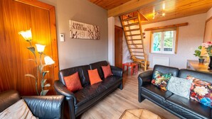 A cozy living room with a black leather sofa, a wooden ladder, and a painting on the wall. - Pretty Holiday Home near Durbuy & La Roche-en-Ardennes (Erezee)