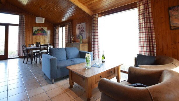 A spacious living room with a wooden ceiling, a blue sofa, a brown leather armchair, and a wooden coffee table.