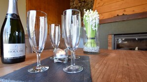 A bottle of Bouché champagne, three champagne flutes, a lit candle, and a vase with flowers on a wooden table.