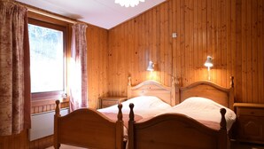 A wooden-paneled bedroom with a double bed, two bedside lamps, and a window with curtains.