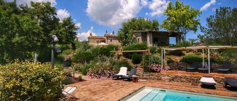 A swimming pool with lounge chairs, a stone building, and lush greenery in the background.