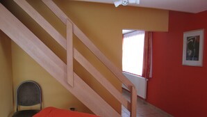Une pièce avec un escalier en bois, une chaise et un lit.