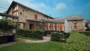 Un bâtiment en pierre doté d’un espace extérieur abrité avec des sièges, d’un barbecue en briques et d’un chemin menant à l’entrée.