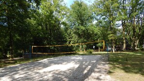 A volleyball court with a net, surrounded by trees.
