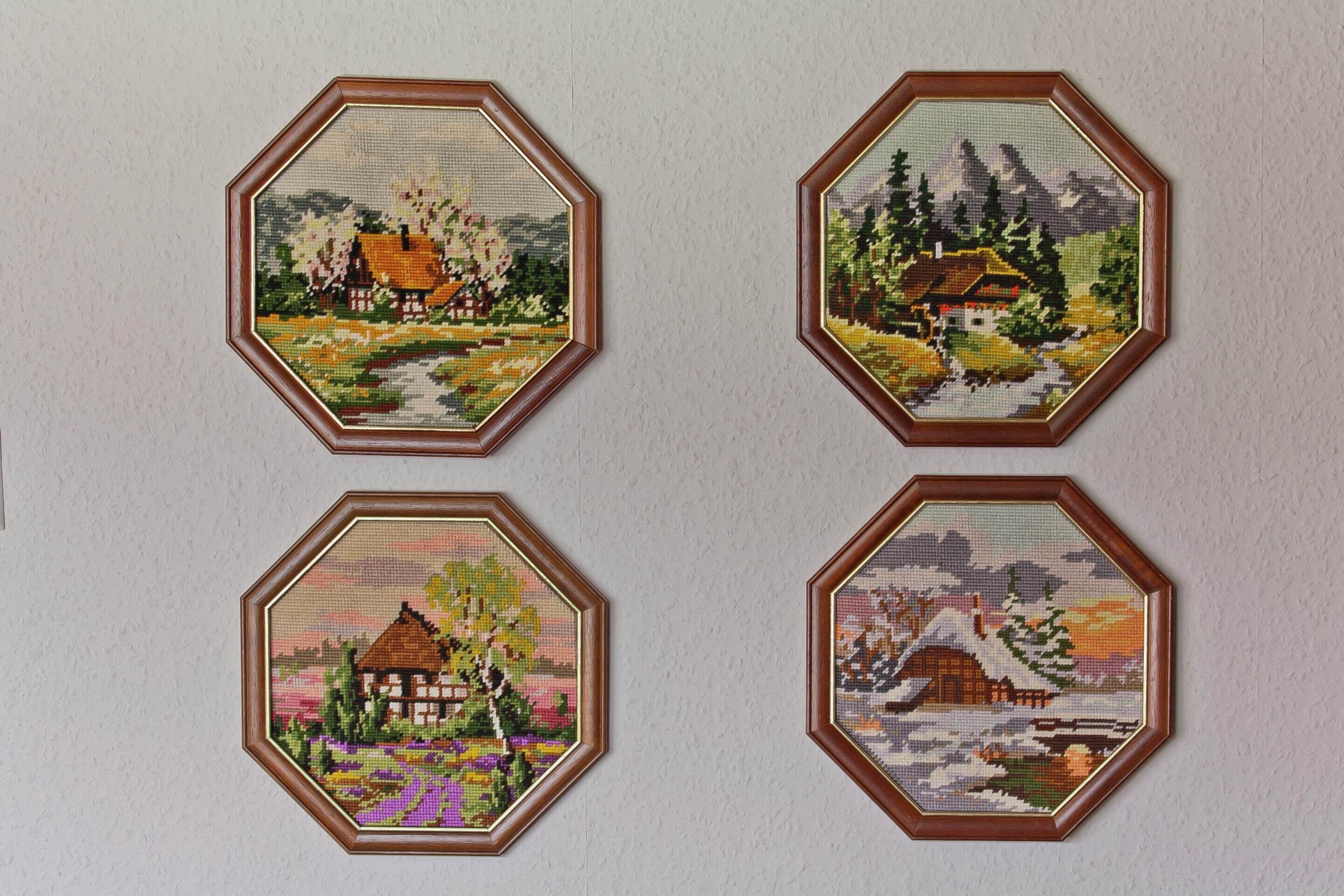 Cuatro obras de arte bordadas a punto de cruz en forma octogonal sobre una pared.