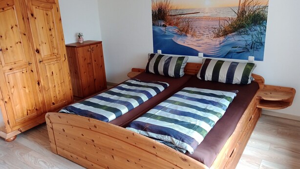 A bedroom with a wooden bed, a wooden wardrobe, and a painting of a beach scene. - Apartment in Leudersdorf, Eifel With Terrace (Üxheim)