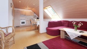 A cozy living room with a red sofa, a wooden dining table with a vase of flowers, and a kitchen in the background. - Apartment in Waldachtal Near the Forest (Waldachtal)