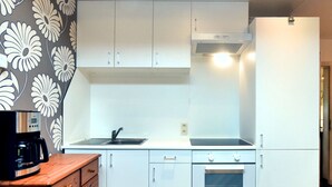 Eine kompakte Küche mit weißen Schränken, einem eingebauten Backofen, einer Kaffeemaschine auf einer Holz Arbeitsplatte und einer Wand mit Muster.