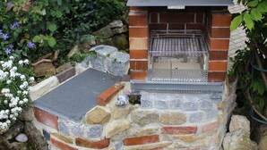 A brick-built outdoor grill with a metal grate and a stone base, surrounded by greenery. - Apartment in the Middle of Franconian Switzerland (Kunreuth)
