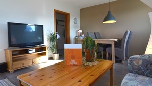 A living room with a television, wooden coffee table, and a dining area with chairs and a table. - Apartment in the Middle of Franconian Switzerland (Kunreuth)