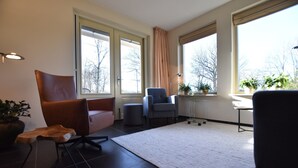 A modern living room with a large window, a brown leather chair, a grey armchair, and a small wooden table. - Rural Holiday Home With Terrace (Zuidwolde)