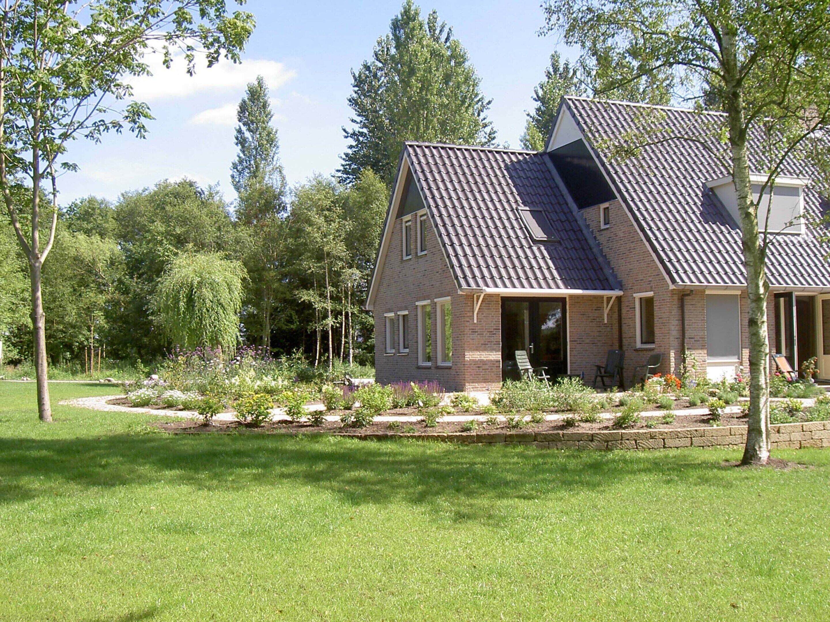 A two-story house with a sloped roof, brick exterior, and a well-maintained garden with various plants and a lawn.