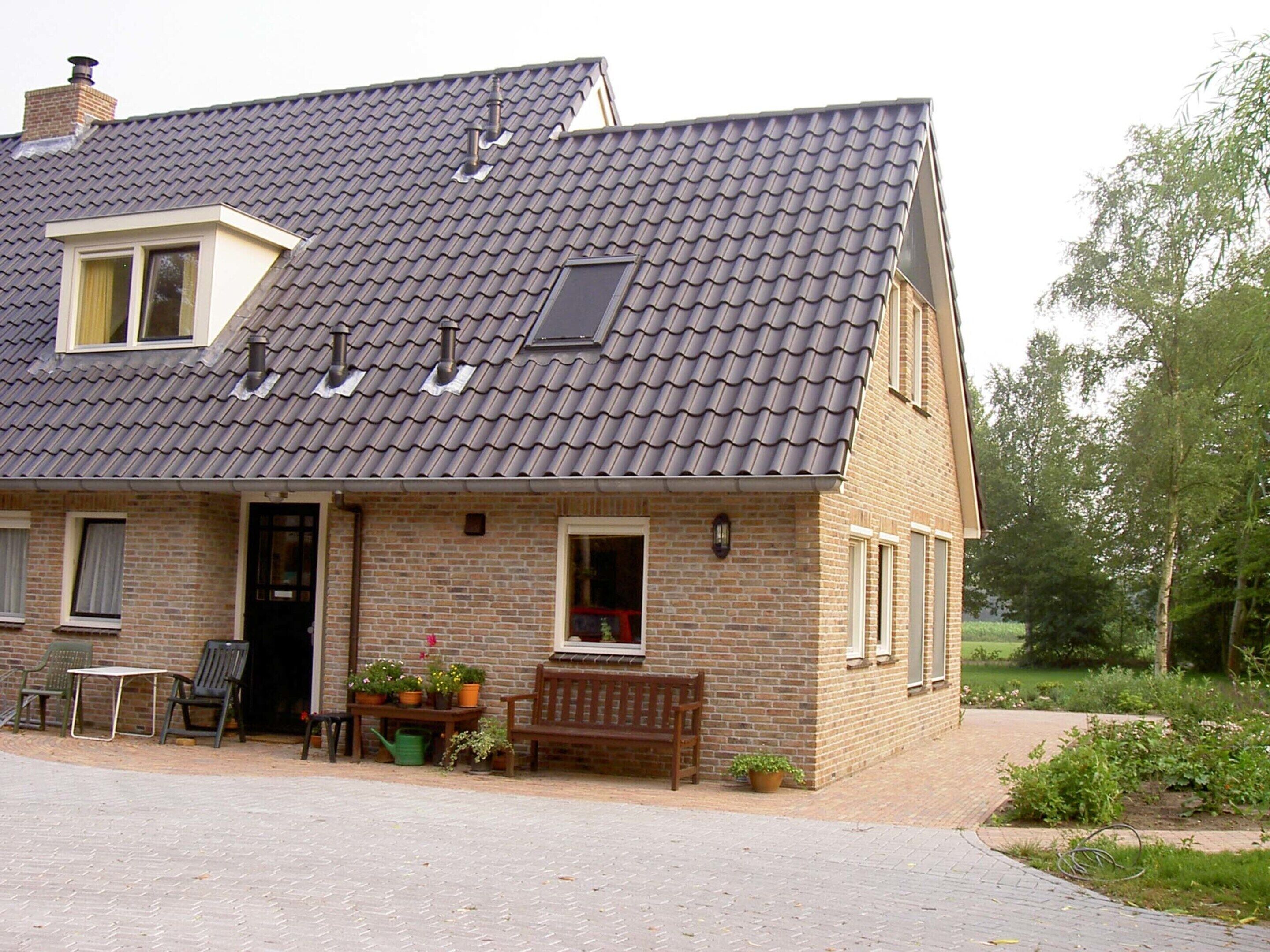 A two-story house with a tiled roof, a front porch with a bench, and potted plants.