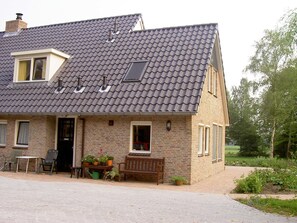 Et toetagers hus med tegltag, en veranda med bænk og plantekasser.