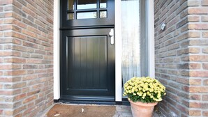A black door with a window above it, a doormat, and a potted plant with yellow flowers. - Rural Holiday Home With Terrace (Zuidwolde)