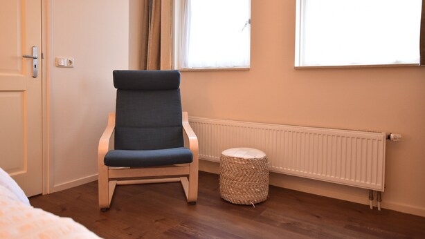A room with a blue chair, a small woven stool, and a radiator. - Rural Holiday Home With Terrace (Zuidwolde)