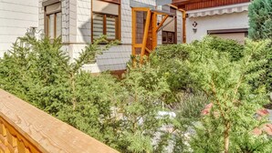 A modern two-story house with a wooden exterior, a wooden staircase leading to the upper floor, and a well-maintained garden with various shrubs and trees.