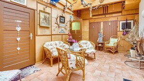 A cozy room with wooden walls, a tiled floor, wicker furniture, and various decorations including antlers and framed pictures.