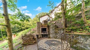 An outdoor patio with a stone wall, a metal table with intricate designs, and a rustic wooden structure. - Forest-edge Hideaway, Bouillon (Bouillon)