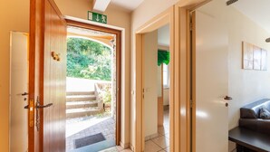 A hotel entrance with a wooden door, a green exit sign, a tiled floor, a bench, and a view of greenery outside. - Forest-edge Hideaway, Bouillon (Bouillon)