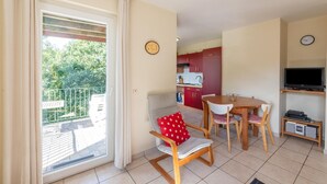 A room with a dining area, a kitchen, a TV, and a balcony with a view of trees. - Forest-edge Hideaway, Bouillon (Bouillon)