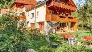 A two-story wooden house with a balcony, a staircase leading to the upper floor, and a garden with outdoor seating. - Rustic Black Forest Getaway (Masserberg)