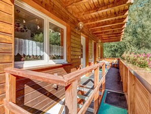 Una cabaña de madera con un porche cubierto, ventanas amplias y vistas a la vegetación.