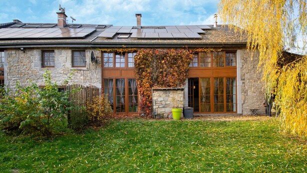 Una casa de piedra con un amplio portón, un porche pequeño y un jardín con césped y hojas caídas.
