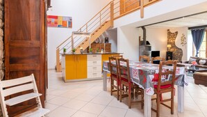Amplia sala de estar con mesa de comedor, sillas de madera y una escalera que conduce a un nivel superior.