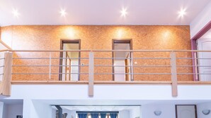 Un interior de varios niveles con una pared de madera texturizada, un balcón con barandilla de metal e iluminación empotrada.