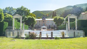 A building with a central pavilion, surrounded by manicured hedges and a grassy area. - Villa in Grimaud Near Tennis Court & Pool (Montbrun-les-Bains)