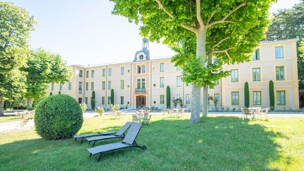 A building with a symmetrical facade, a central entrance, and a well-maintained lawn with lounge chairs. - Villa in Grimaud Near Tennis Court & Pool (Montbrun-les-Bains)