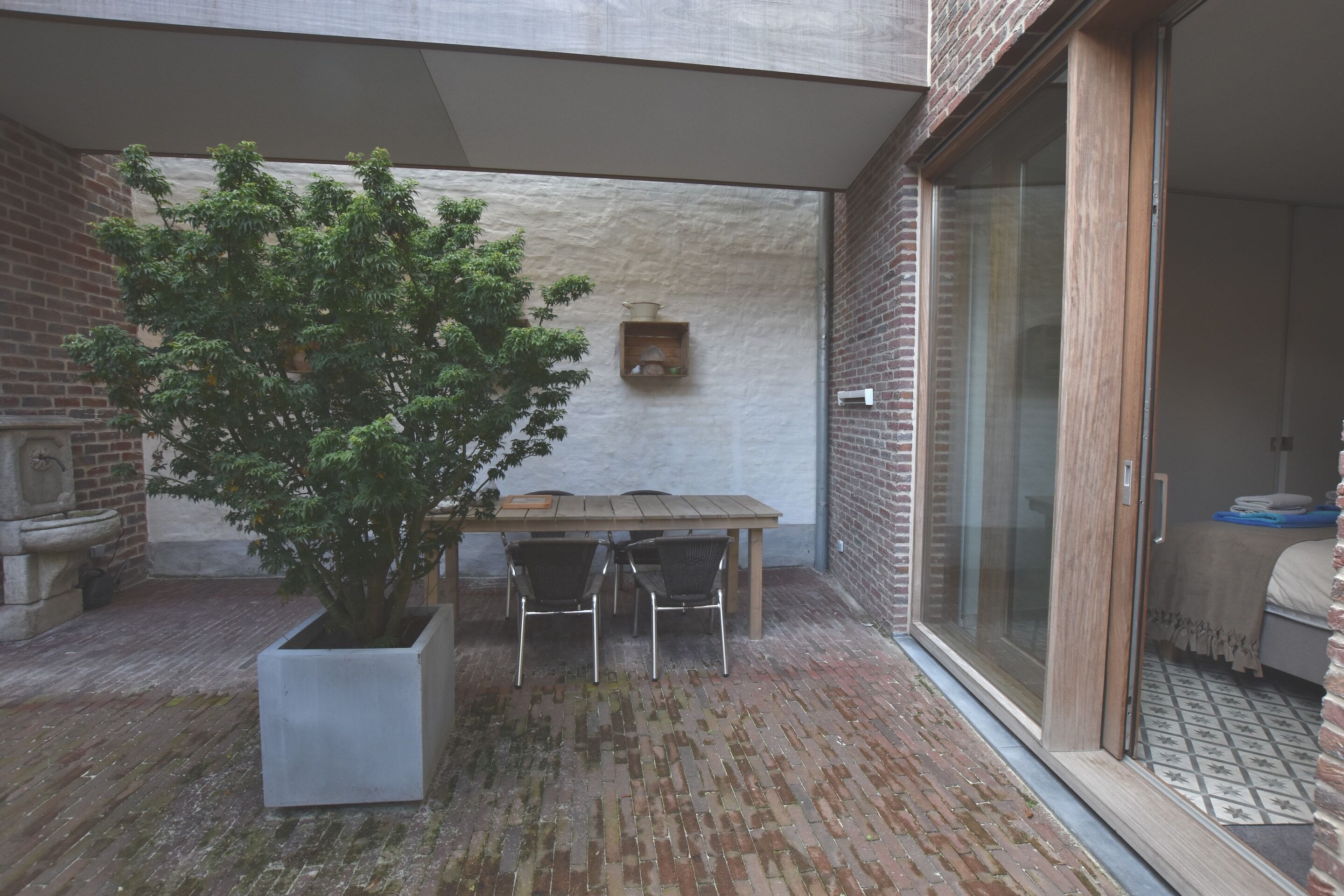 En terrasse med et træbord og stole, en potteplante og en murstensmur.