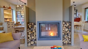 A modern living room with a fireplace, a bookshelf, and a dining area. - Chimay Nature Hideaway (Chimay)