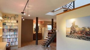 A spacious living area with a bookshelf, a staircase, and a painting on the wall. - Chimay Nature Hideaway (Chimay)