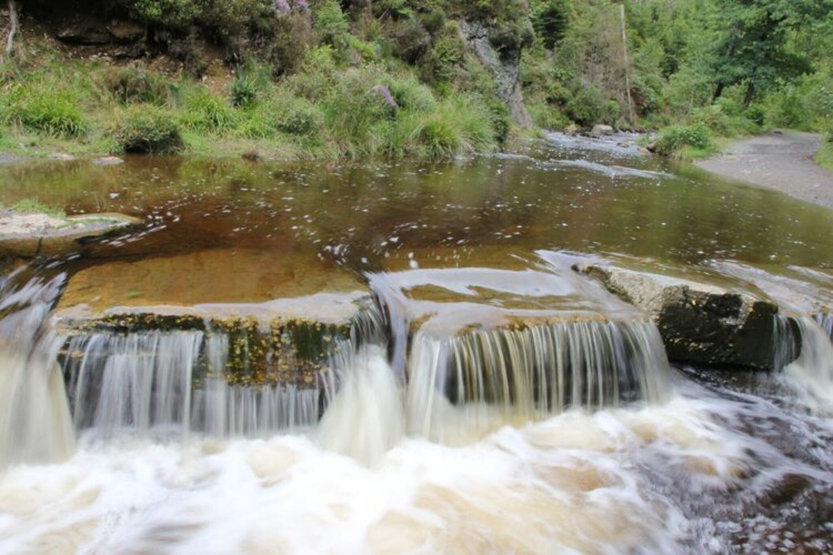 A waterfall in a natural setting with rocks and greenery.