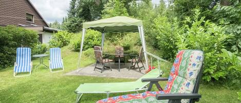 Een terras buiten met een tafel en stoelen, een overdekte zithoek en een ligstoel.