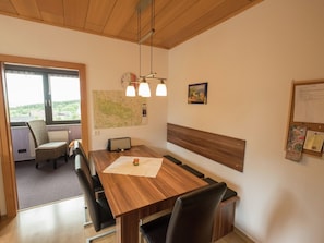 Un coin repas avec une table en bois, des chaises, une carte accrochée au mur, une horloge et un tableau d’affichage où sont affichées des annonces.