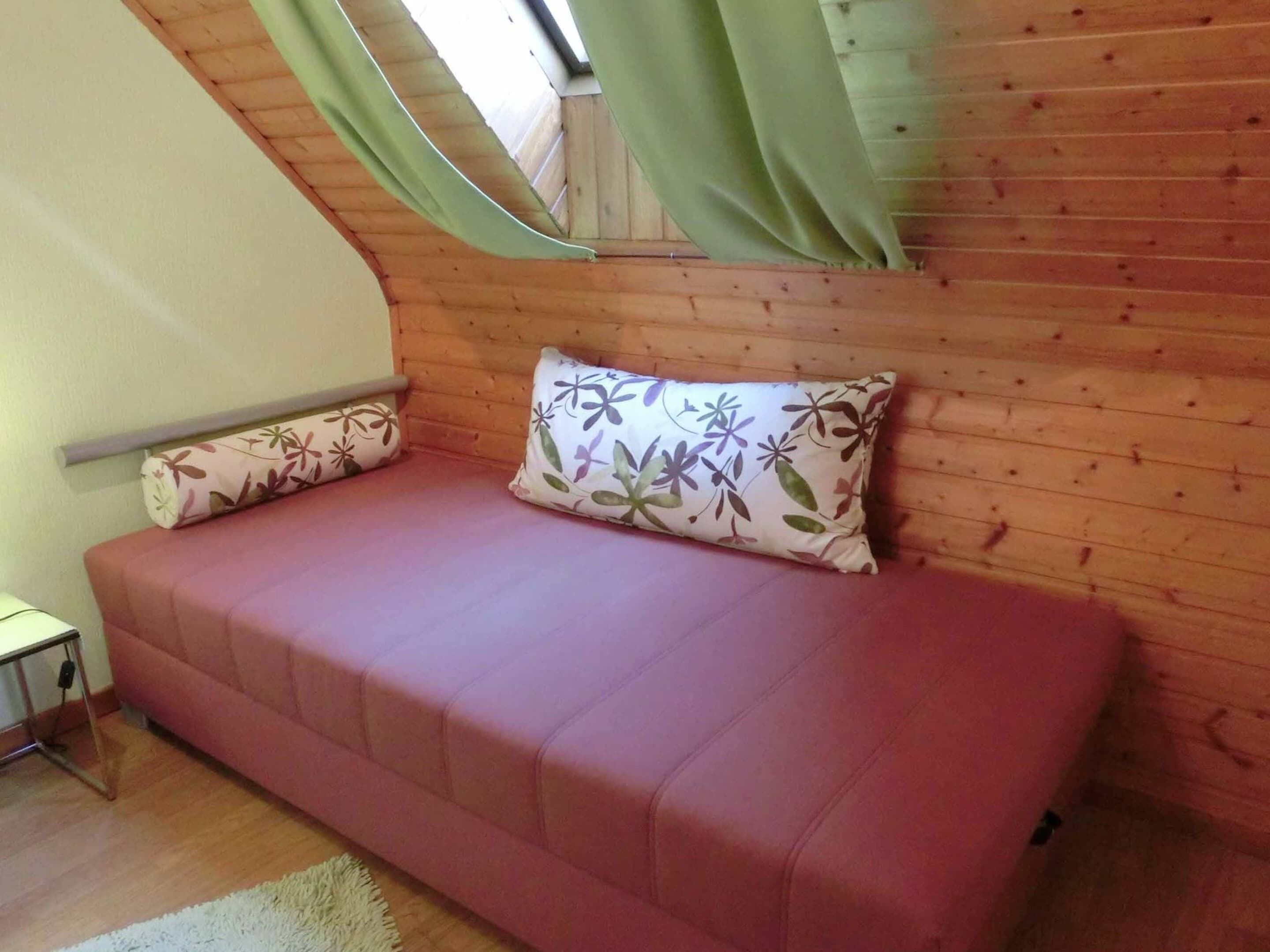 Ein gemütliches Zimmer mit Holzbalkendecke, einem rosafarbenen Sofa und Kissen mit Blumenmuster.
