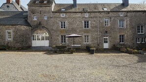 Un bâtiment en pierre avec une cour recouverte de gravier, un espace de repos abrité et une grande entrée en arc de cercle.
