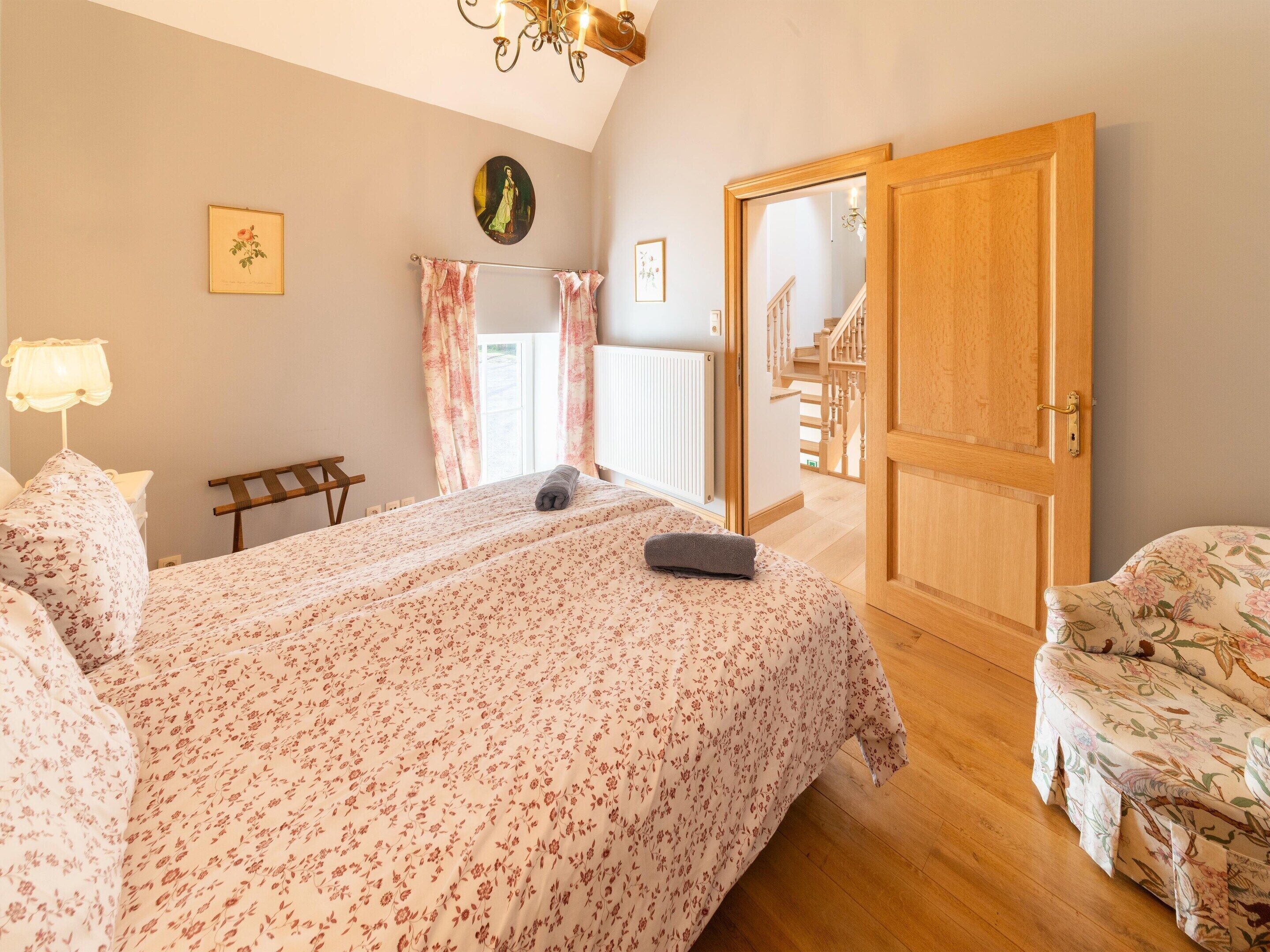 A bedroom with a bed, a chair, a wooden door, and a staircase leading to another room.