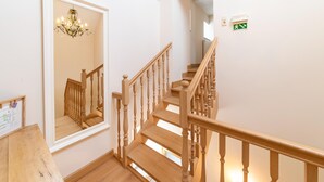 Un escalier en bois avec un miroir qui reflète l’escalier, un lustre et un panneau vert indiquant la sortie de secours.
